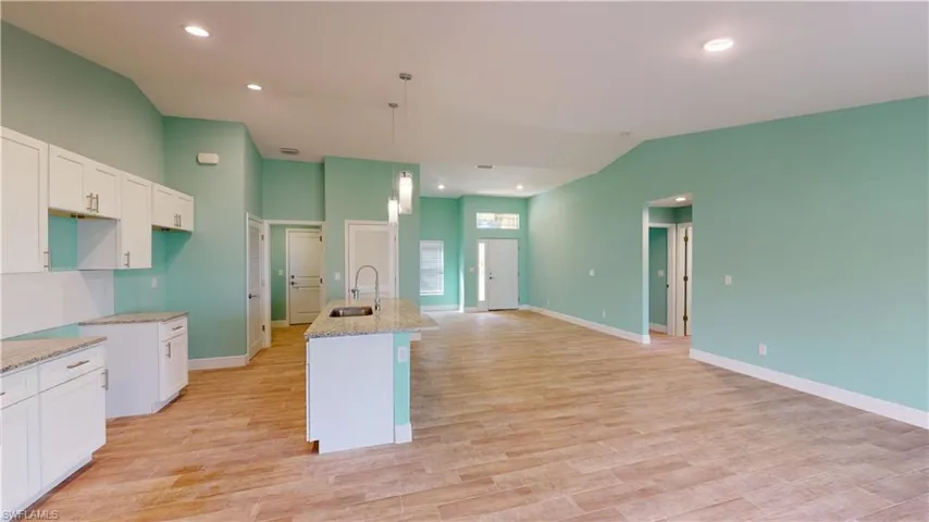 Kitchen featuring white cabinetry, a center island with sink, light stone countertops, light wood-style flooring, and vaulted ceiling