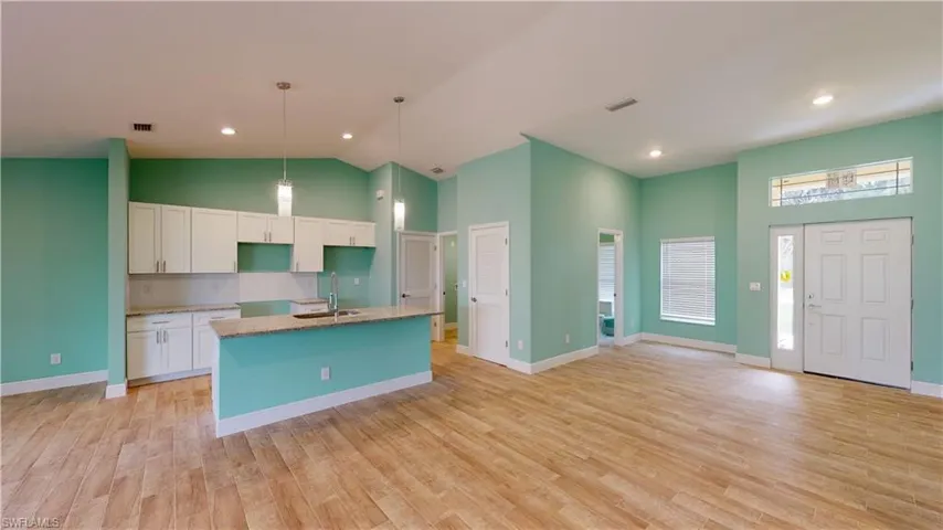 Kitchen featuring white cabinets, a center island with sink, light wood-style floors, hanging light fixtures, and light stone countertops