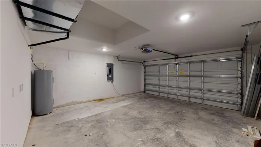 Garage featuring concrete block wall, water heater, electric panel, a garage door opener, and recessed lighting