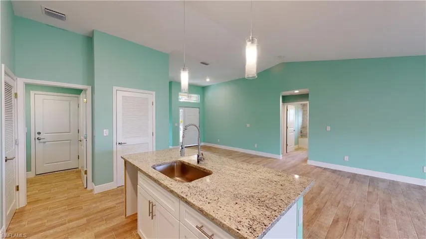 Kitchen with white cabinets, light stone counters, light wood finished floors, a center island with sink, and lofted ceiling