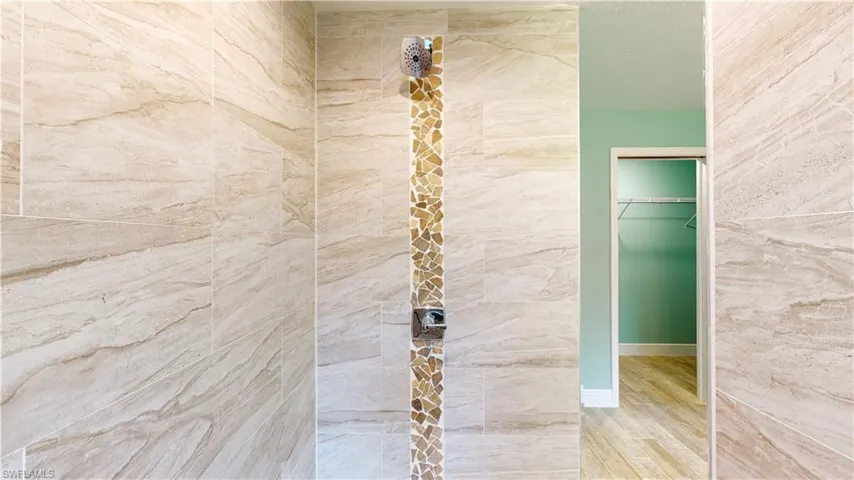 Full bathroom featuring tiled shower, a spacious closet, and light wood-style floors