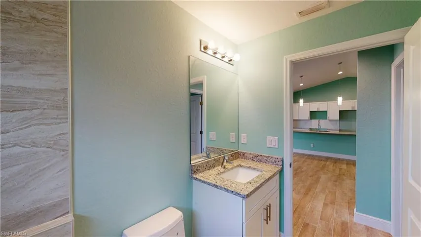 Bathroom with vanity, a textured wall, light wood-style flooring, and lofted ceiling