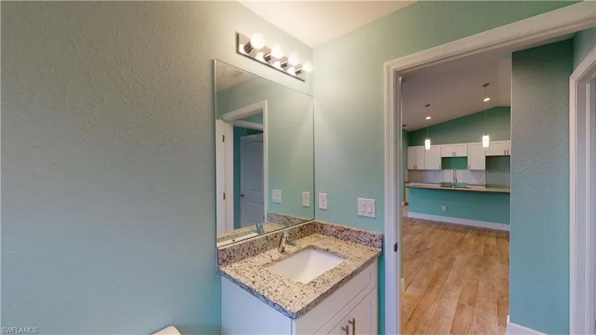 Bathroom featuring a textured wall, vanity, light wood-style floors, and lofted ceiling
