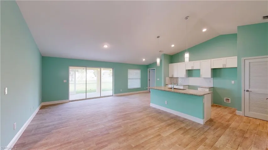 Kitchen with an island with sink, lofted ceiling, light stone counters, light wood-style flooring, and hanging light fixtures