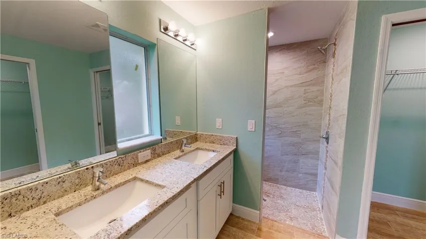 Bathroom featuring a spacious closet, tiled shower, double vanity, and light wood finished floors