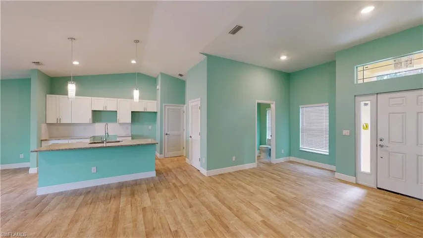 Kitchen with white cabinets, an island with sink, decorative light fixtures, light wood-type flooring, and vaulted ceiling