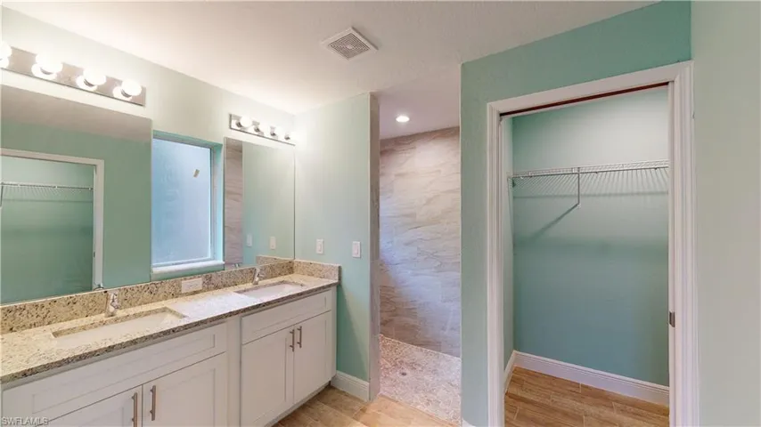 Full bathroom featuring a walk in closet, double vanity, a walk in shower, and light wood-type flooring