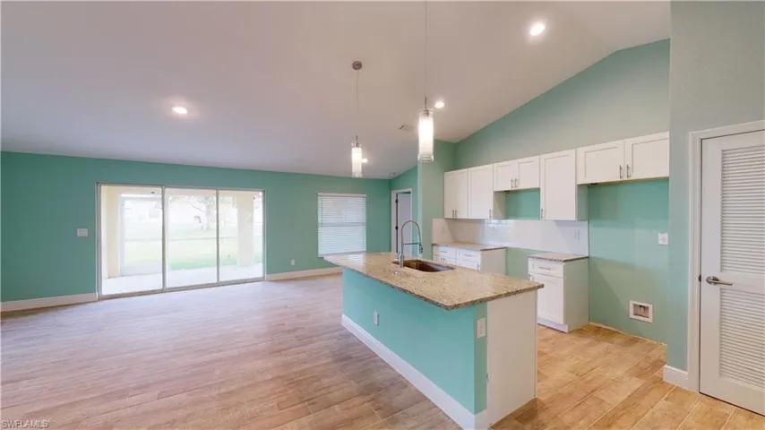 Kitchen featuring lofted ceiling, white cabinets, light stone counters, a kitchen island with sink, and decorative light fixtures
