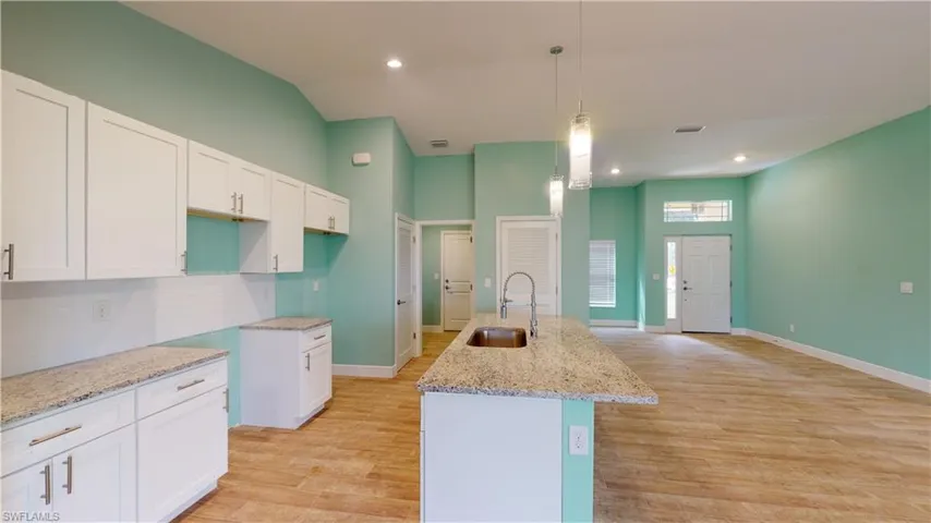 Kitchen featuring white cabinetry, light stone counters, an island with sink, light wood finished floors, and pendant lighting