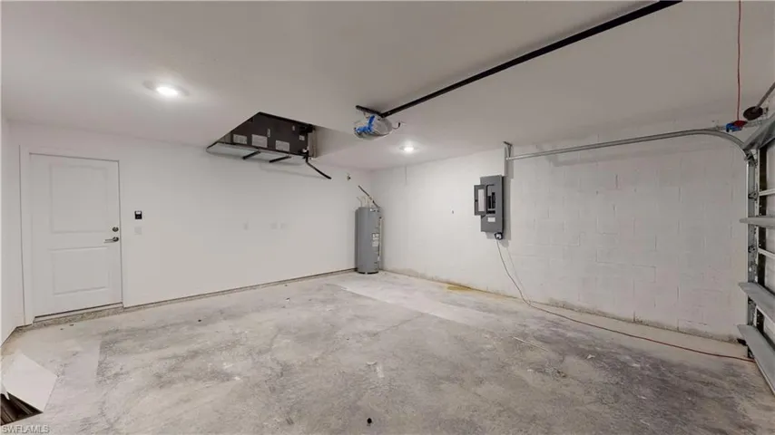 Garage with concrete block wall, electric panel, water heater, and a garage door opener