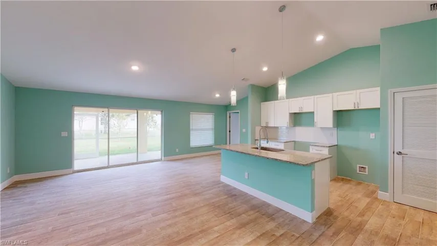 Kitchen featuring light stone counters, white cabinets, a kitchen island with sink, lofted ceiling, and decorative light fixtures