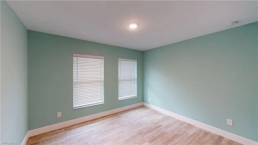 Empty room with light wood-style floors and a smoke detector