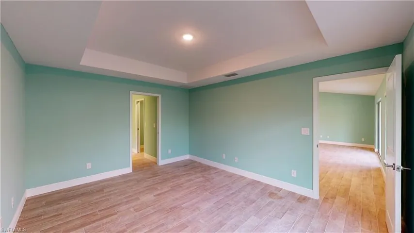 Empty room with light wood finished floors and a tray ceiling