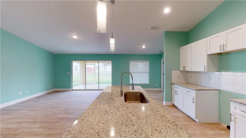 Kitchen featuring white cabinets, light stone countertops, light wood finished floors, hanging light fixtures, and tasteful backsplash