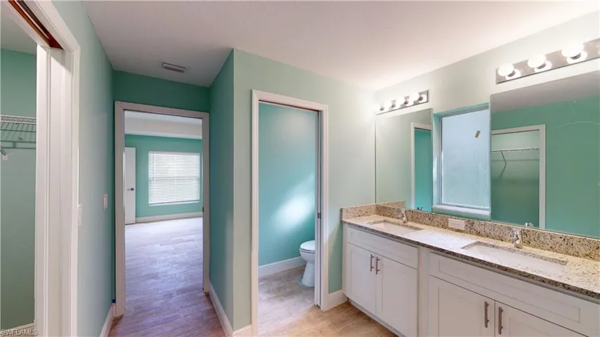 Full bathroom with a spacious closet, double vanity, and light wood-style floors