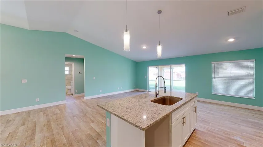 Kitchen featuring white cabinets, light stone countertops, light wood finished floors, open floor plan, and pendant lighting