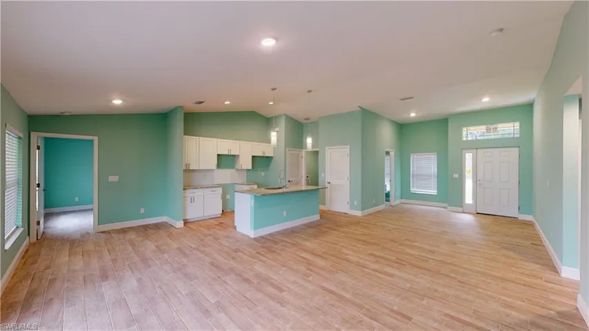 Kitchen featuring white cabinets, an island with sink, hanging light fixtures, open floor plan, and light wood-style flooring