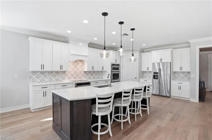 Dual tone kitchen featuring crown molding, two tone cabinetry, stainless steel appliances, a center island with sink, and a kitchen bar