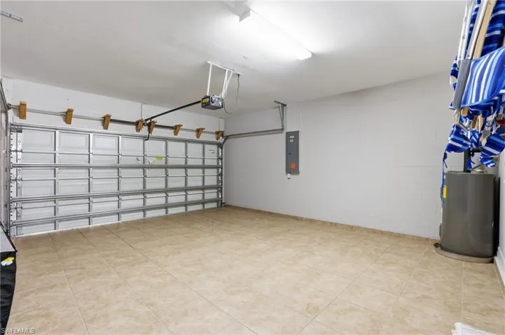 Garage featuring tile floor, electric panel, concrete block wall, and a garage door opener