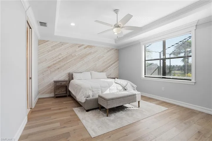 Bedroom featuring wooden walls, an accent wall, light wood-type flooring, a ceiling fan, and ornamental molding