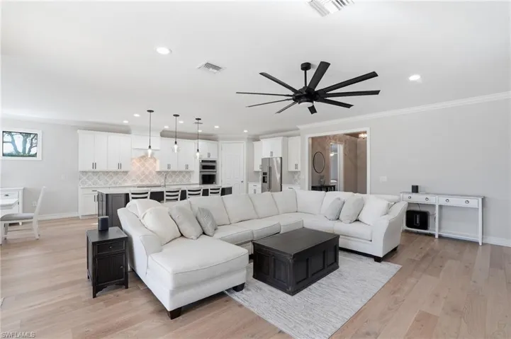 Living room featuring light wood-type flooring, crown molding, recessed lighting, and ceiling fan