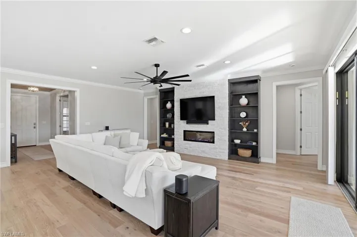 Living room featuring crown molding, light wood-type flooring, ceiling fan, built in shelves, and recessed lighting