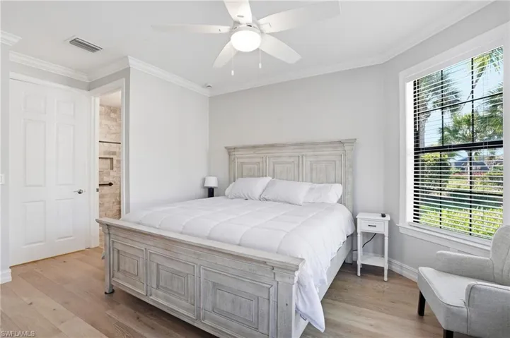 Bedroom with ornamental molding, light wood-type flooring, ensuite bath, and ceiling fan