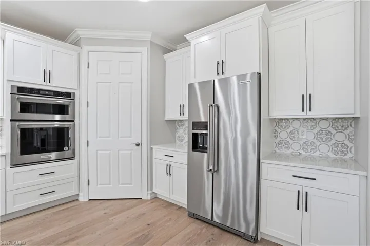 Kitchen featuring stainless steel appliances, crown molding, white cabinetry, decorative backsplash, and light wood-type flooring