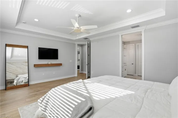 Bedroom with a raised ceiling, light wood-style floors, crown molding, recessed lighting, and a ceiling fan