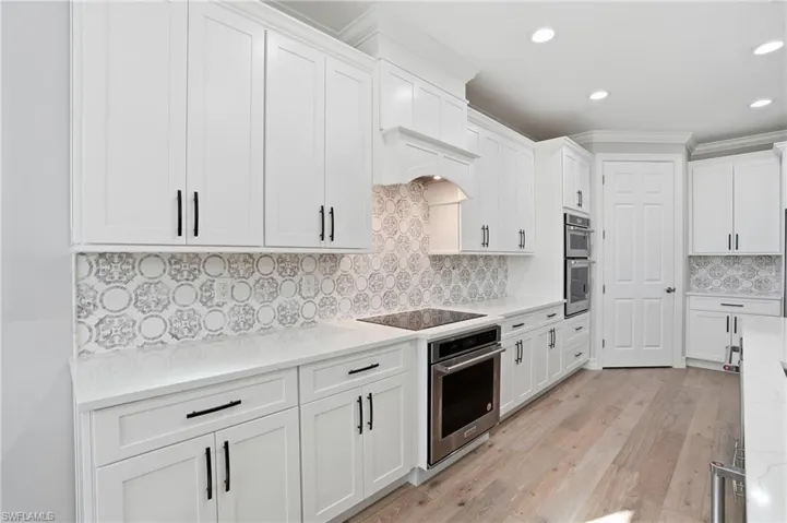 Kitchen with white cabinets, light stone countertops, light wood finished floors, recessed lighting, and ornamental molding