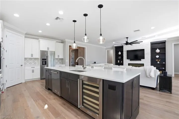 Kitchen with wine cooler, decorative light fixtures, ornamental molding, an island with sink, and two tone color scheme