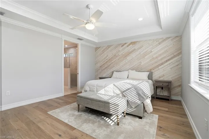 Bedroom featuring wooden walls, an accent wall, light wood finished floors, ceiling fan, and crown molding