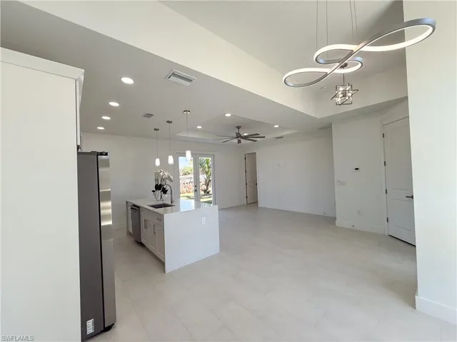 Kitchen with pendant lighting, a tray ceiling, stainless steel appliances, open floor plan, and white cabinets