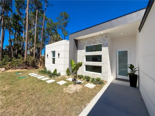 View of exterior entry featuring a lawn, stone siding, and stucco siding
