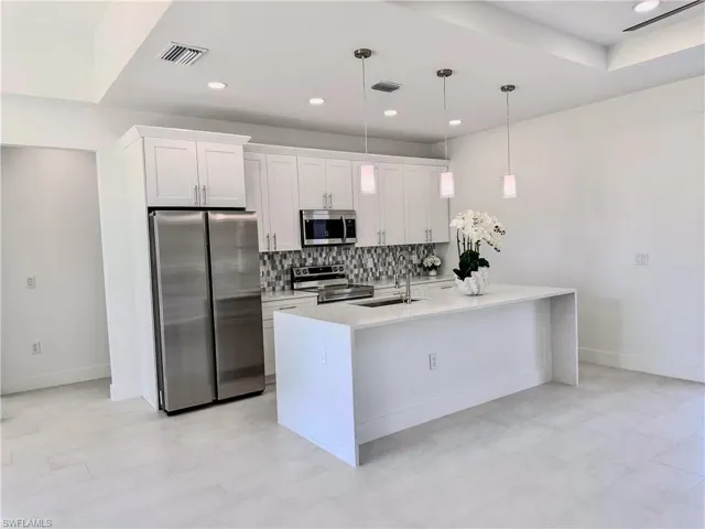 Kitchen with stainless steel appliances, light stone countertops, white cabinetry, a kitchen island with sink, and backsplash