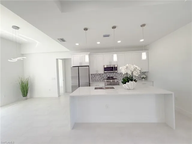 Kitchen with light stone countertops, white cabinets, stainless steel appliances, and hanging light fixtures