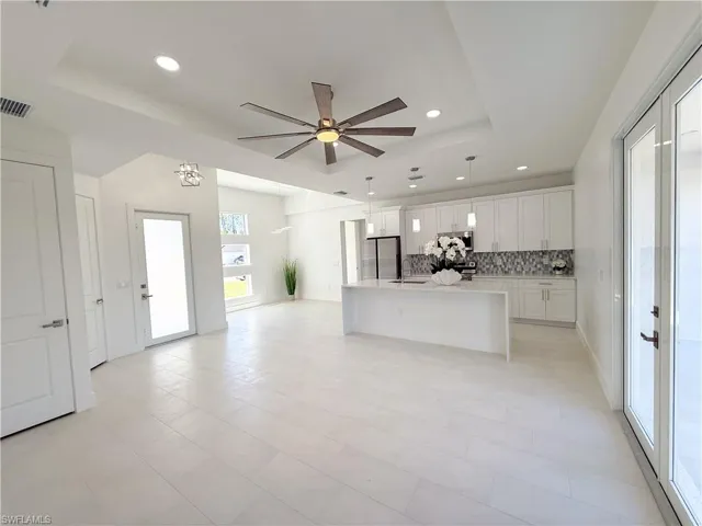 Kitchen featuring white cabinets, a center island with sink, a tray ceiling, ceiling fan, and decorative backsplash