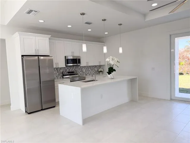 Kitchen featuring stainless steel appliances, light stone countertops, backsplash, white cabinetry, and an island with sink