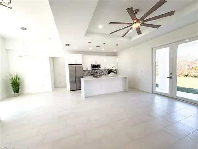Kitchen with stainless steel appliances, open floor plan, a ceiling fan, white cabinets, and a tray ceiling