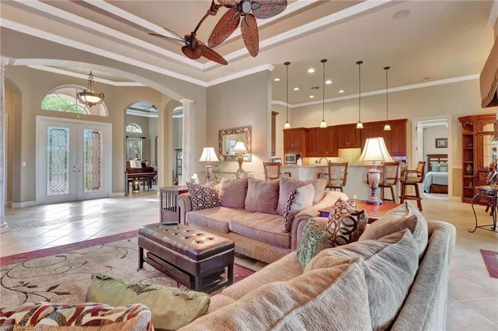 Living area featuring arched walkways, light tile patterned floors, decorative columns, and a ceiling fan