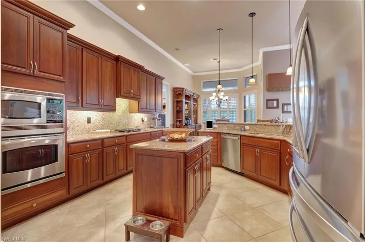 Kitchen with ornamental molding, tasteful backsplash, appliances with stainless steel finishes, an inviting chandelier, and light tile patterned floors