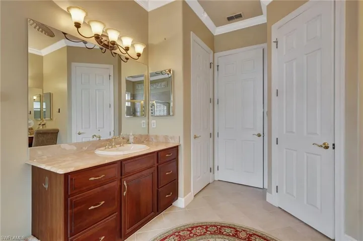 Bathroom with vanity, tile patterned flooring, baseboards, visible vents, and ornamental molding
