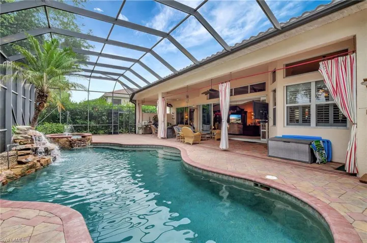 View of swimming pool with glass enclosure, ceiling fan, a pool with connected hot tub, and a patio area
