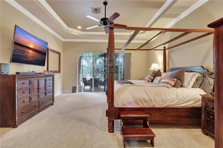 Carpeted bedroom featuring a tray ceiling, ornamental molding, baseboards, access to exterior, and visible vents