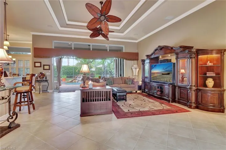 Living room with a tray ceiling, light tile patterned floors, ornamental molding, and a ceiling fan