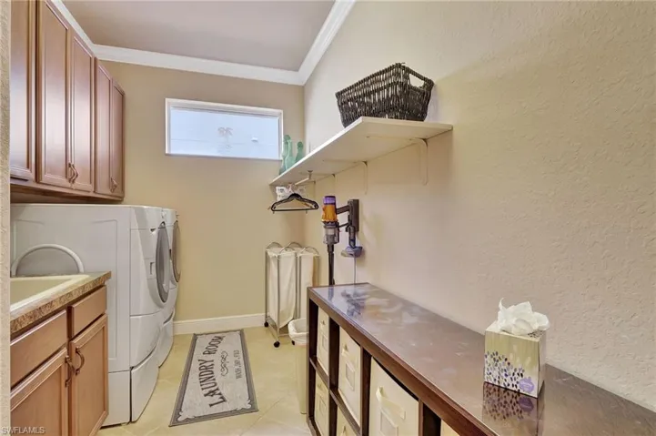 Washroom featuring crown molding, light tile patterned floors, baseboards, separate washer and dryer, and cabinet space