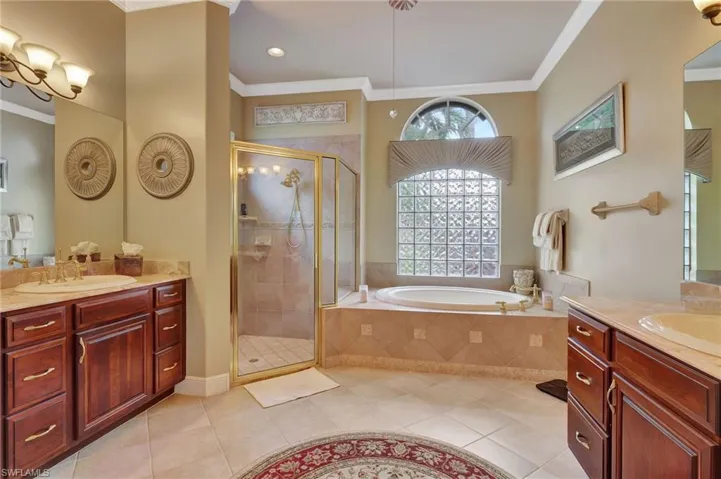 Bathroom featuring a bath, ornamental molding, tile patterned floors, two vanities, and a stall shower