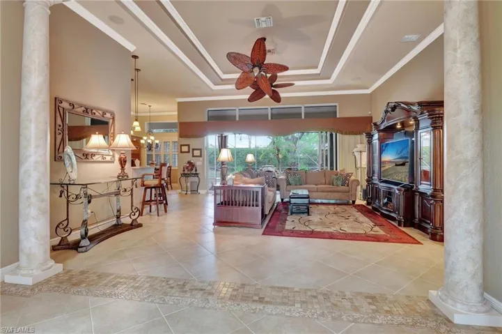 Living room featuring ornamental molding, ceiling fan, decorative columns, and a raised ceiling