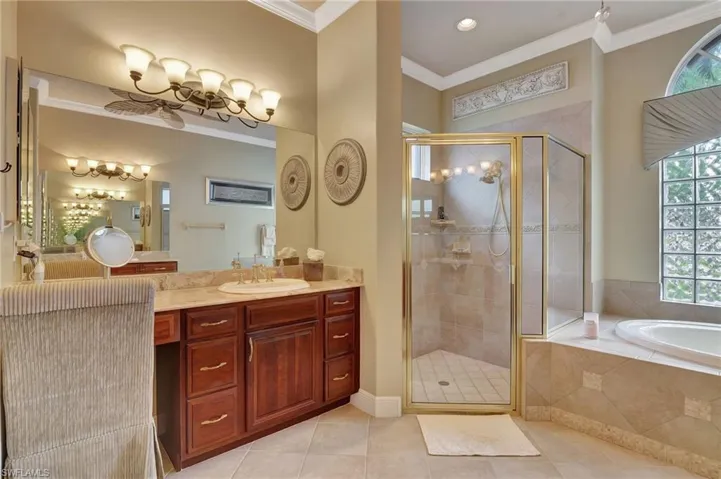 Full bath featuring a notable chandelier, crown molding, vanity, a shower stall, and tile patterned flooring