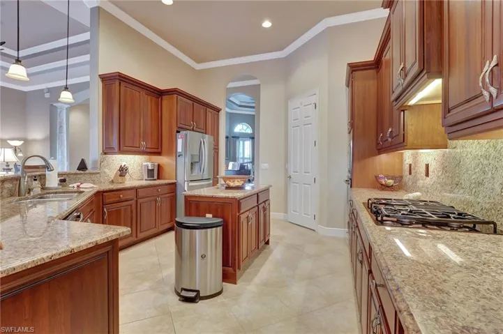 Kitchen featuring stainless steel refrigerator with ice dispenser, gas cooktop, a sink, arched walkways, and light stone counters